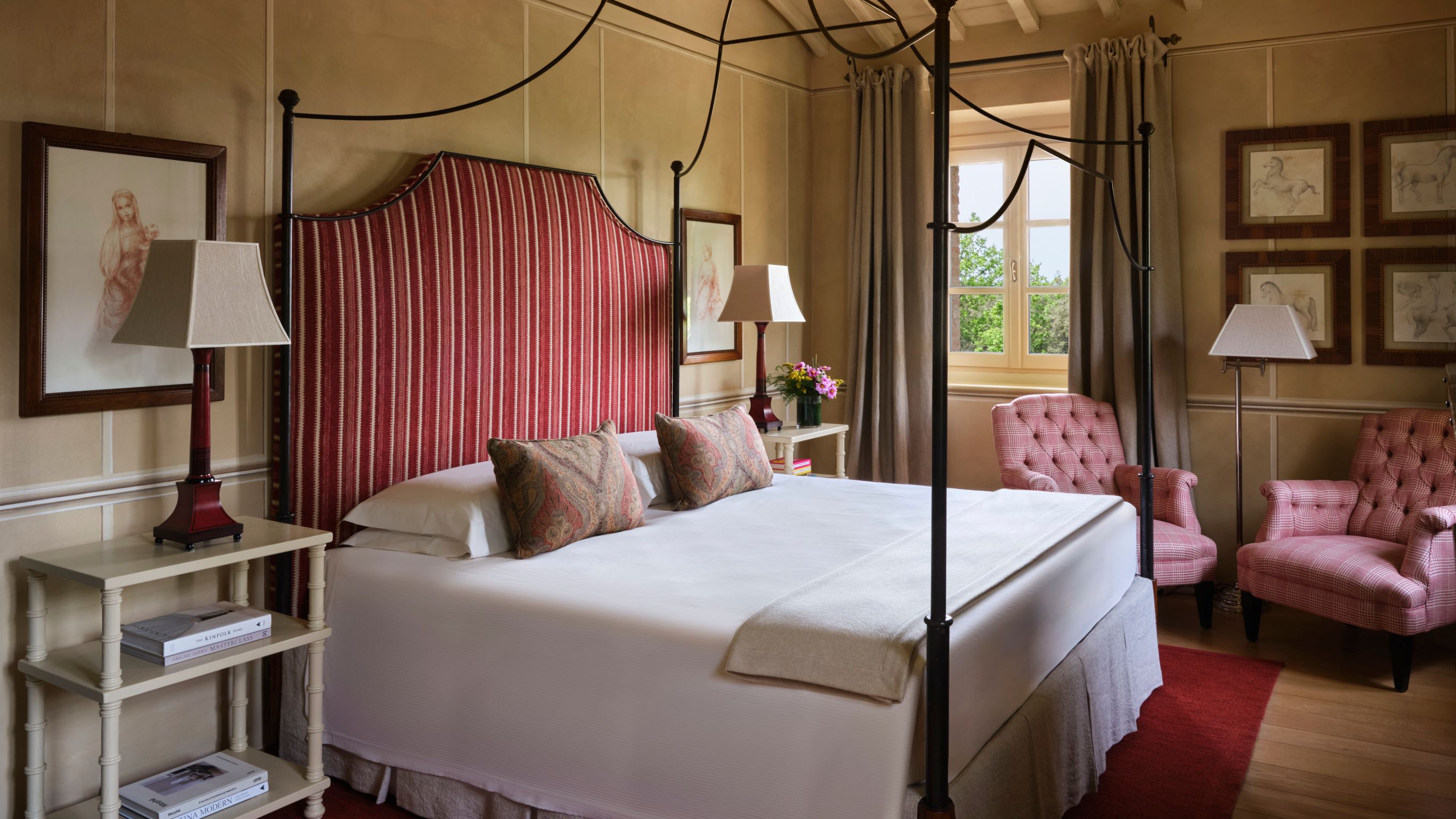 Hotel bedroom with a four-poster bed, a red  headboard and pink armchairs